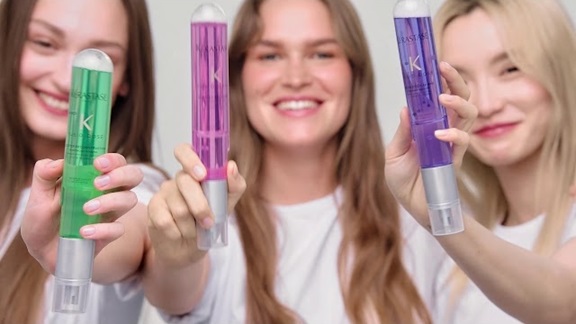 Tre giovani donne sorridenti mostrano prodotti di bellezza in flaconi colorati, in un ambiente luminoso e vivace.
